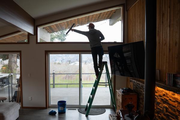 TOPRUNG cleaner high on a ladder cleaning transom windows above large glass doors inside a beautiful home