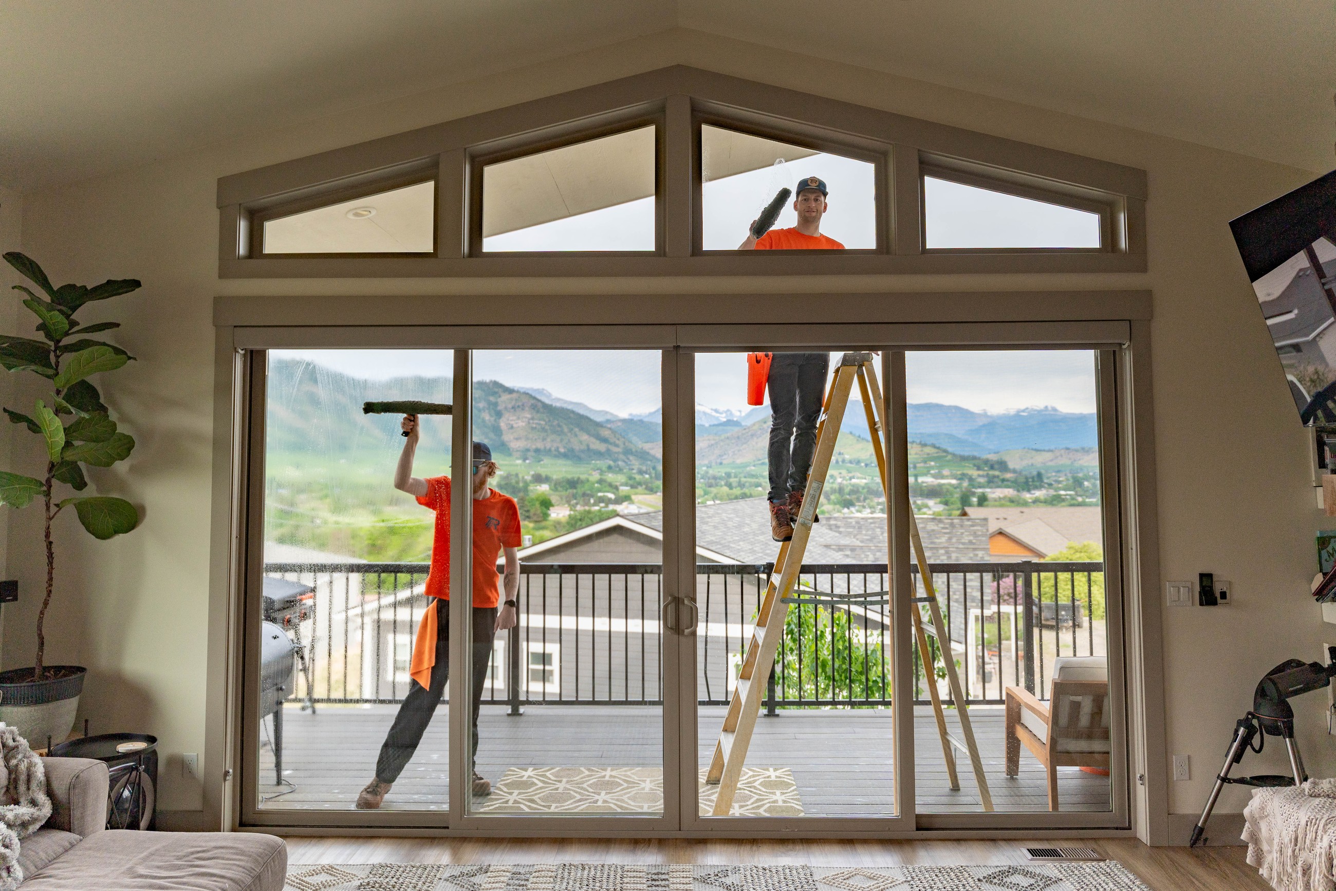 TOPRUNG technician cleaning a large wall of windows inside a bright residential home